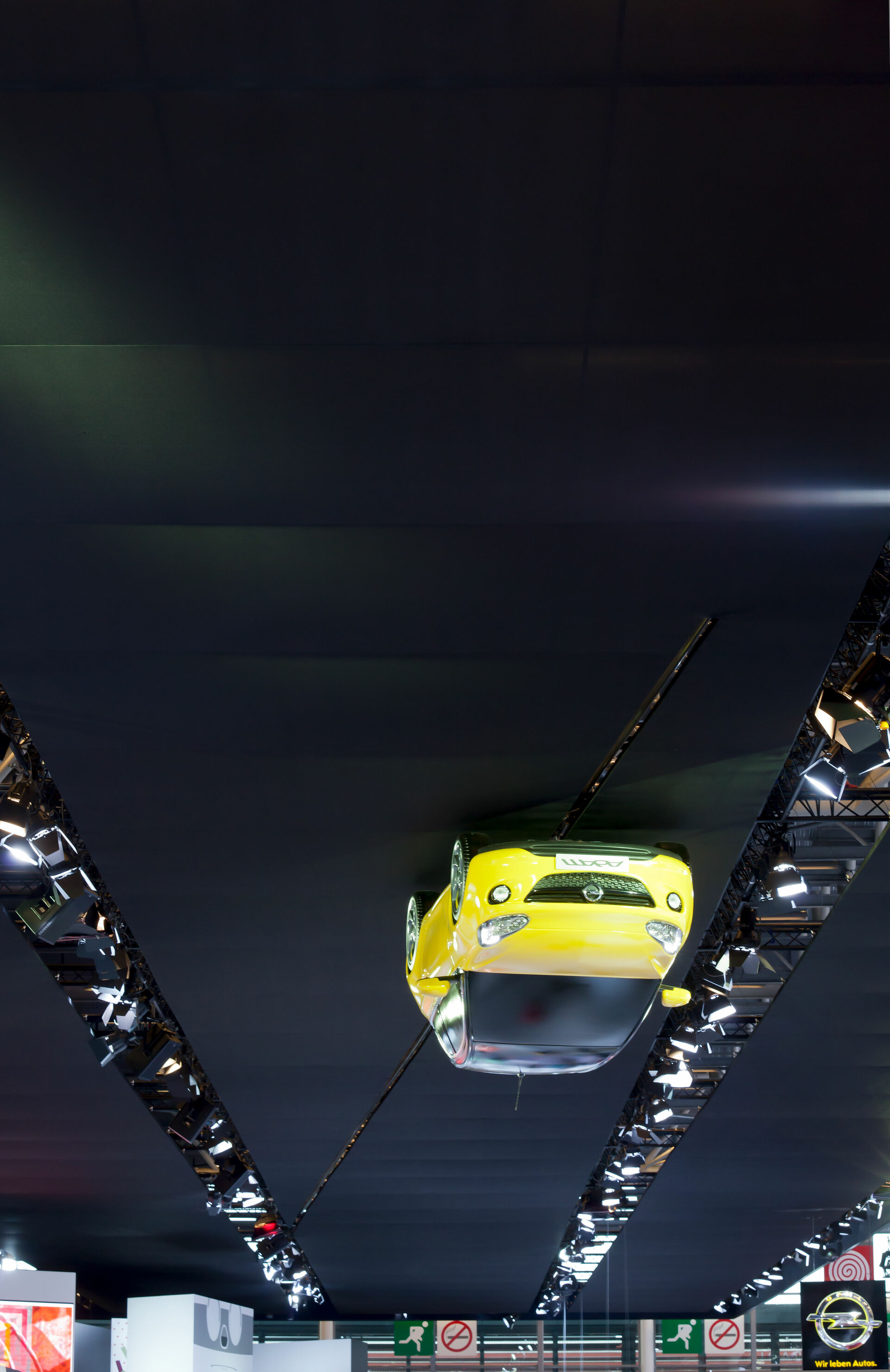 Schwarze Stoffdecke in Messehalle mit gelben Kleinwagen über Kopf darauf fahrend